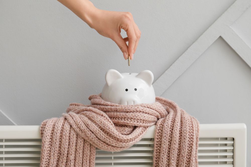 A person is putting a coin into a piggy bank wrapped in a scarf.