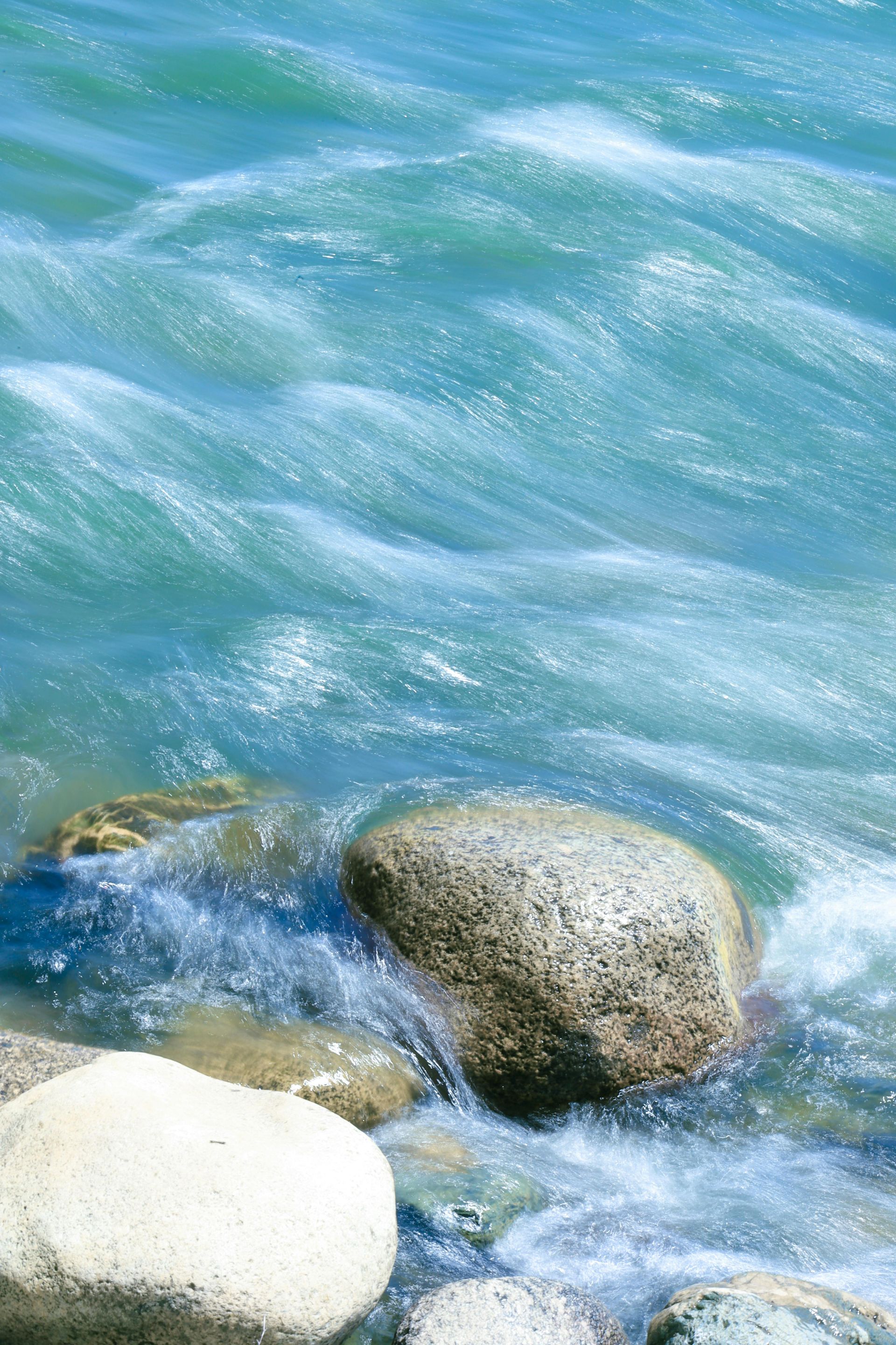 Water cascading over rocks; teal-colored water; sunlit, outdoors.