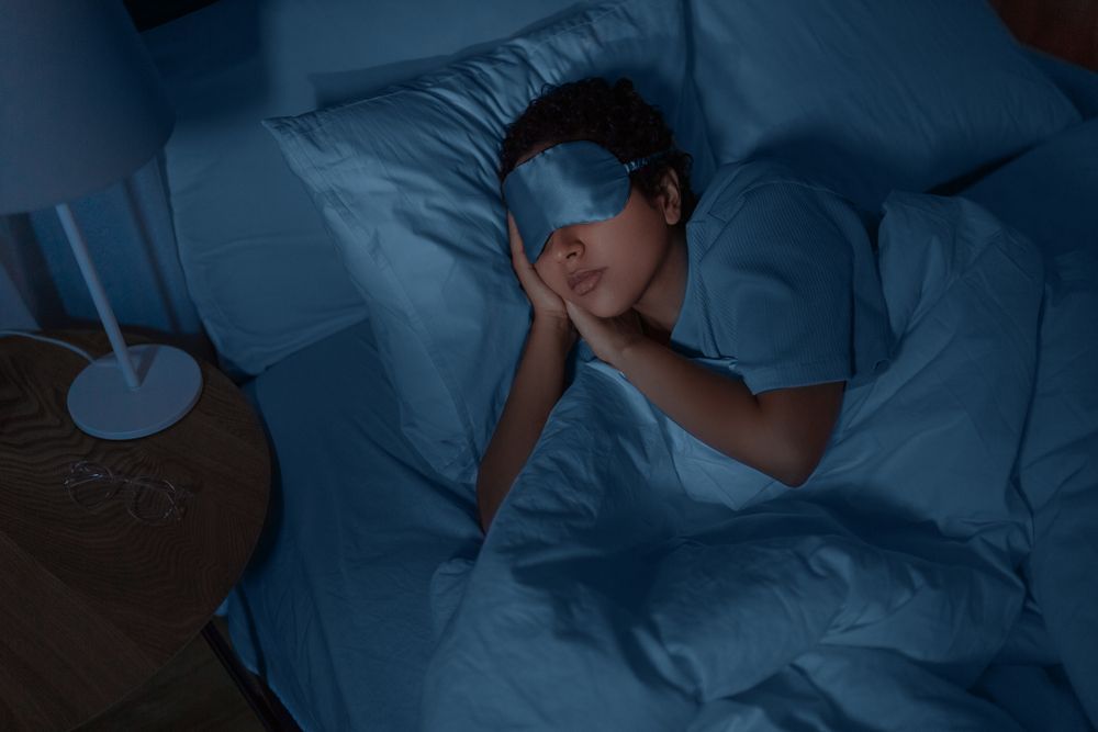 A woman is sleeping in a bed with a sleep mask on her eyes.