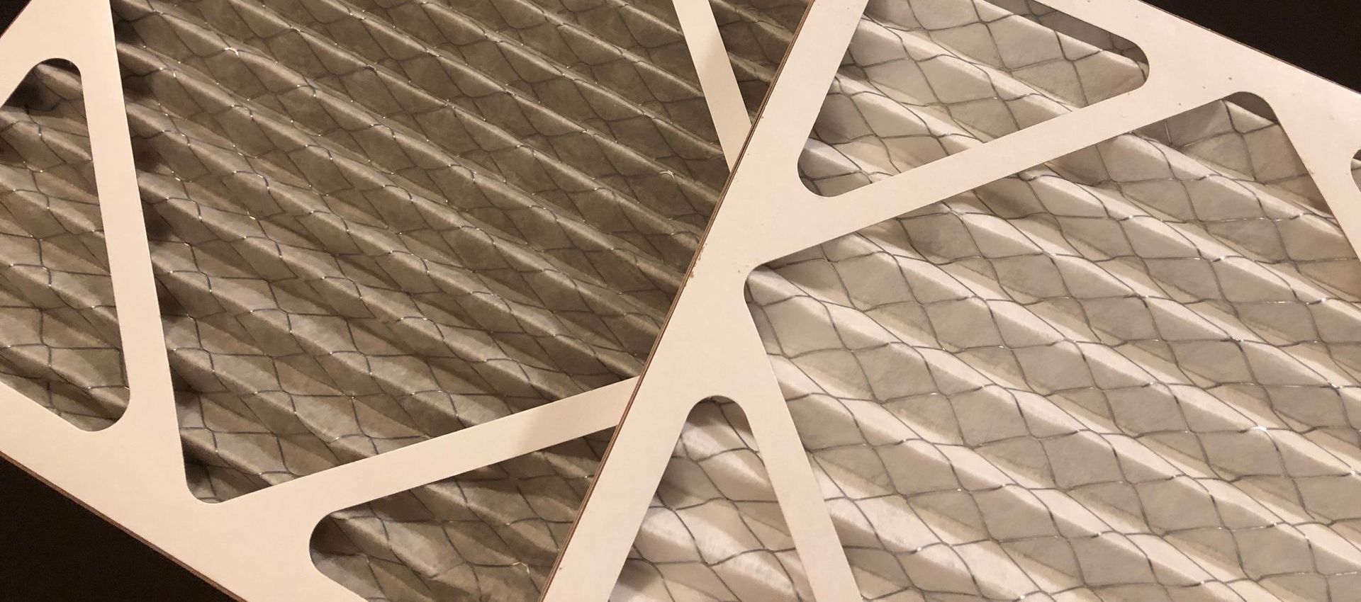 Two furnace air filters; one dirty, one clean. Both are constructed of pleated, corrugated material within a cardboard frame.