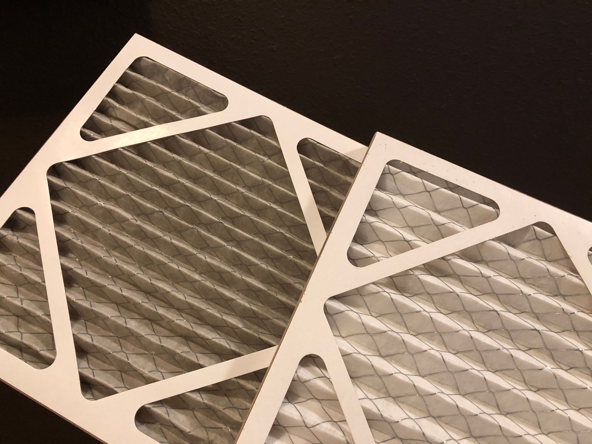 Two rectangular air filters, one dirty and one clean, are placed against a black background.