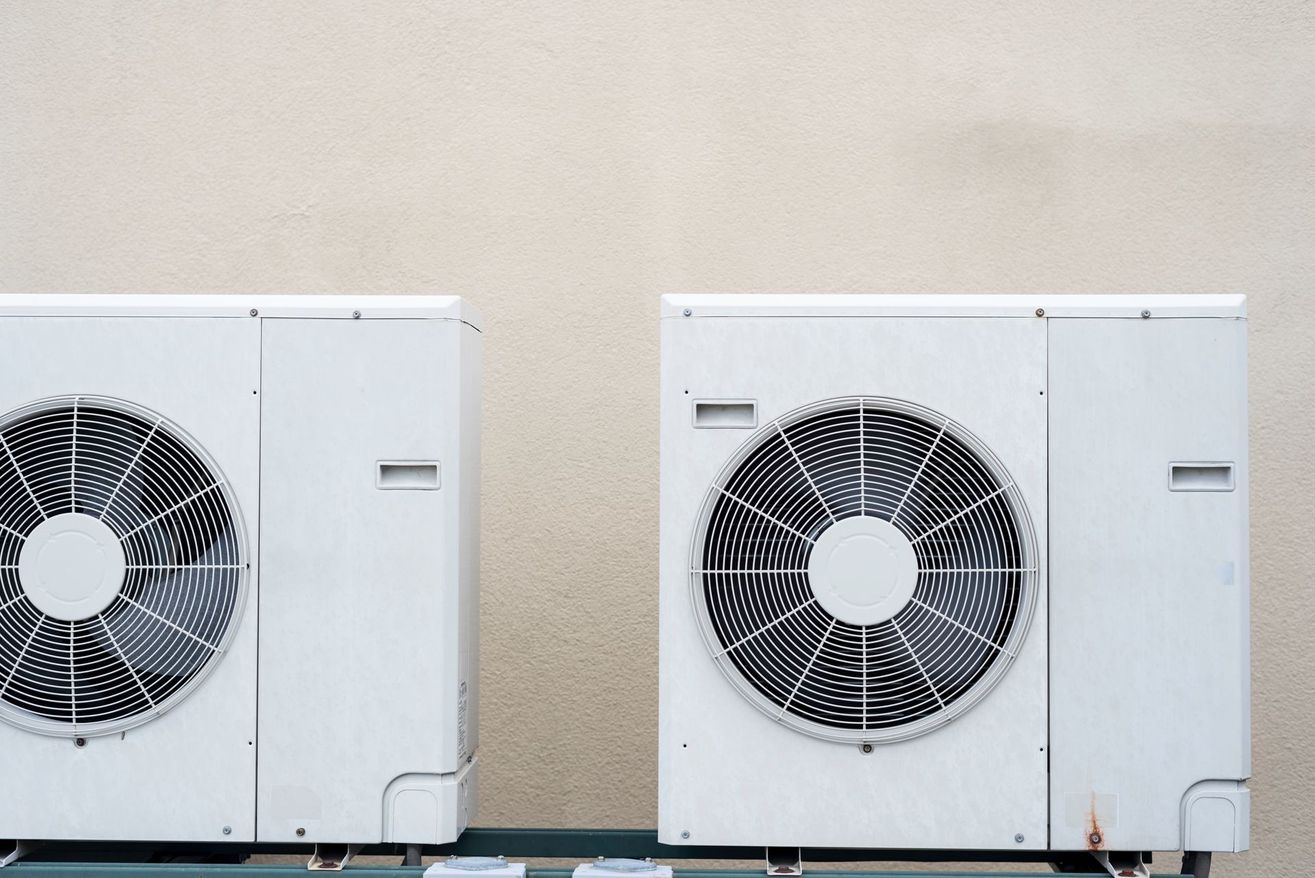 Two white air conditioning units mounted on a wall, with large fans visible.