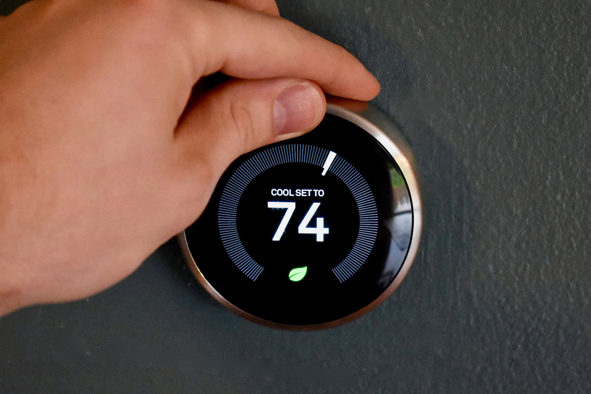 Hand adjusting a smart thermostat displaying 74 degrees. The screen shows 