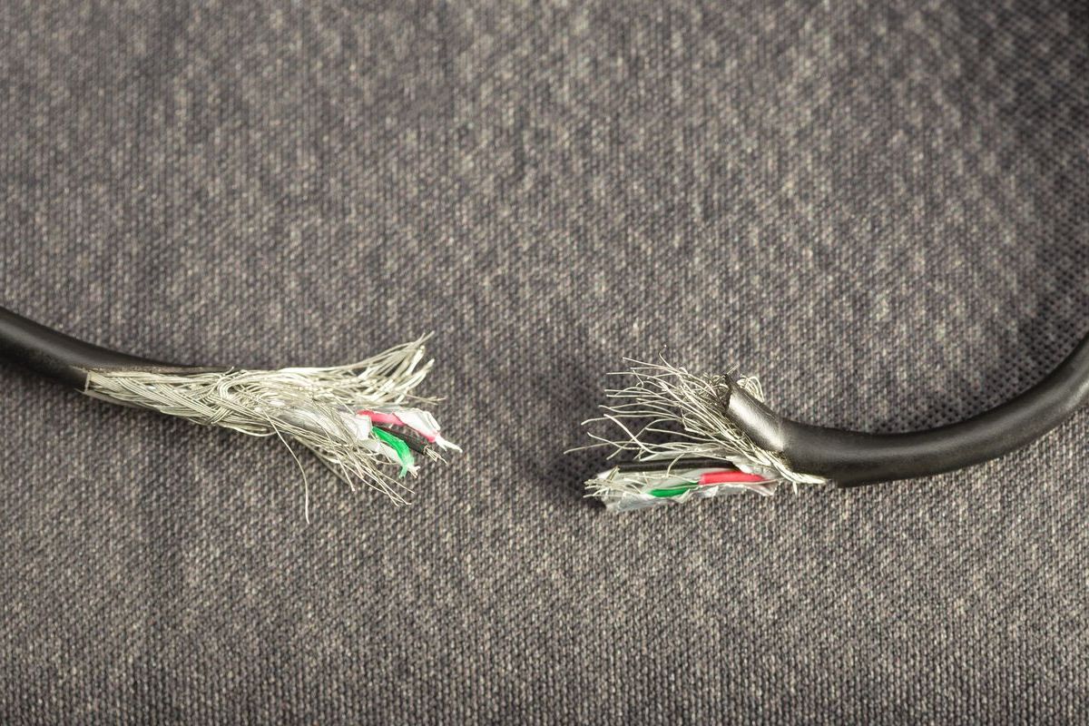 Severed black cable on a gray background, exposing colored wires inside. The cable is torn apart.