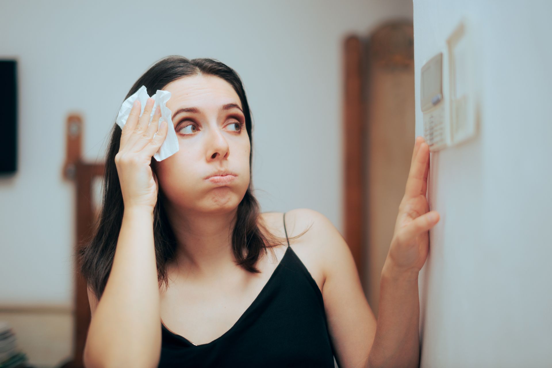 A woman is wiping her face with a napkin while looking at a light switch.