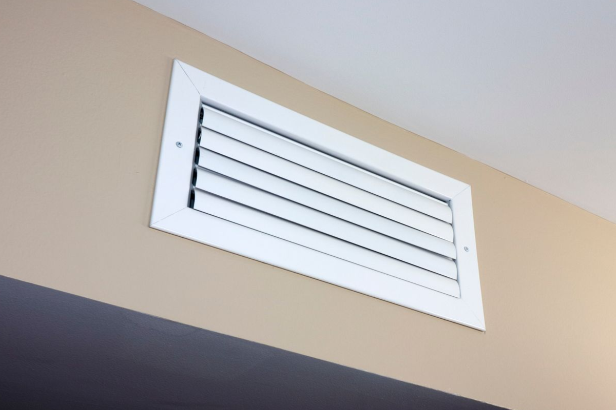 White air vent on a beige wall near a ceiling.