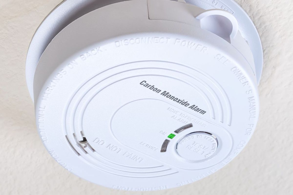 Carbon monoxide alarm on a ceiling, white with a green light indicating it is working.