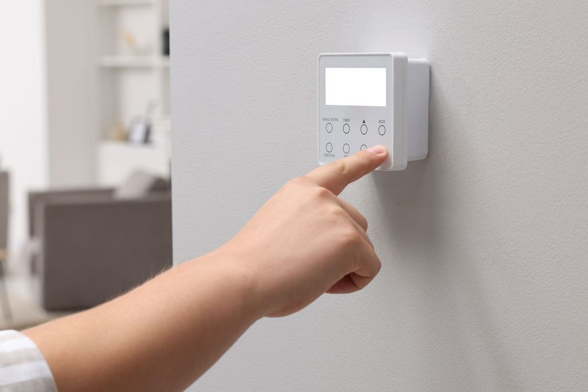 A person is pressing a button on a security system on a wall.
