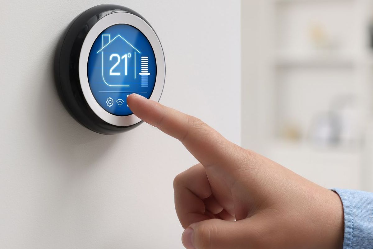 A person is pressing a button on a smart thermostat.