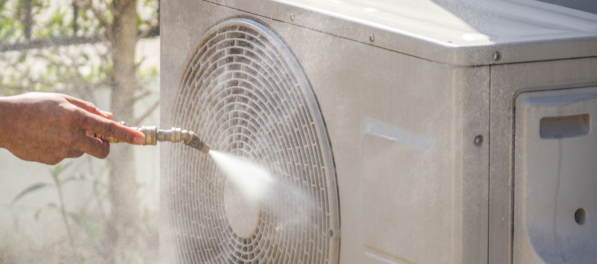 Person using a hose to spray clean an outdoor air conditioning unit.