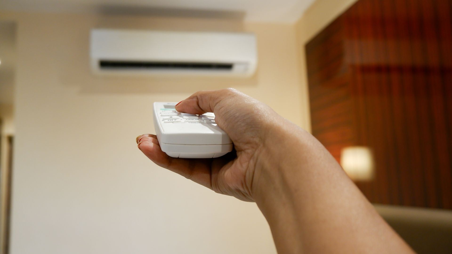 A person is holding a remote control in front of an air conditioner.