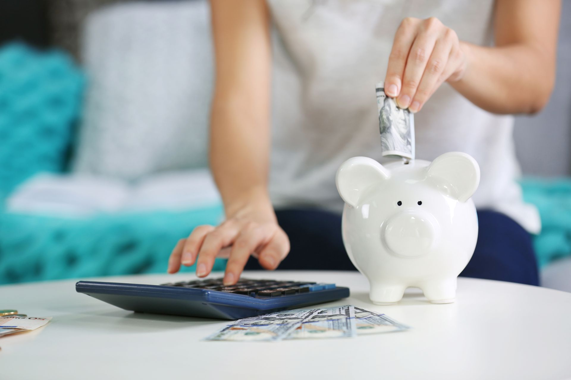A woman is putting money into a piggy bank while using a calculator.