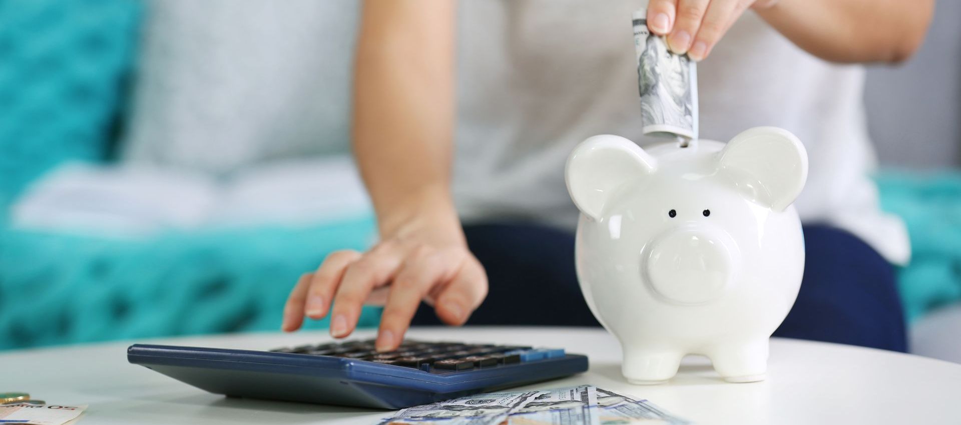 A woman is putting money into a piggy bank while using a calculator.