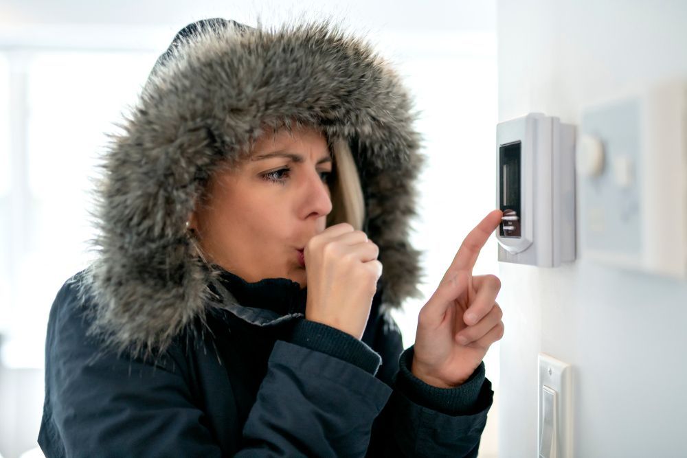 A woman in a fur coat is adjusting a thermostat.