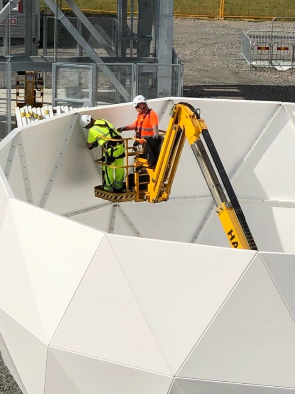 Two workers in a cherry picker inside an upturned satellite antenna dome
