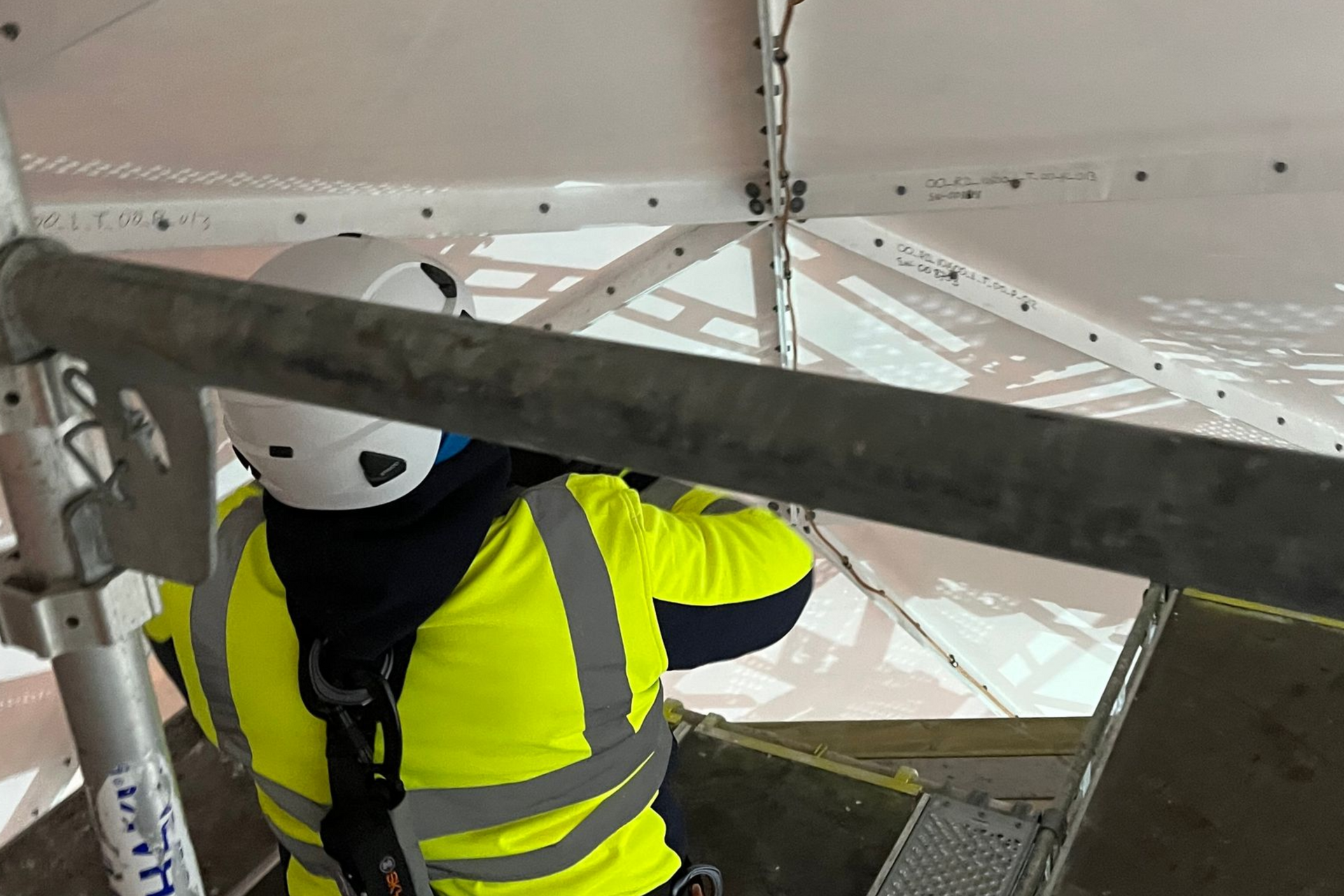 Close up view behind a worker in high vis jacket, who is looking at the underside of an antenna dish.