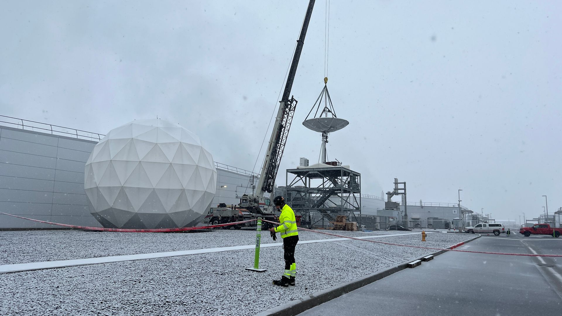 Crane lifting antenna into place with engineer in foreground. 