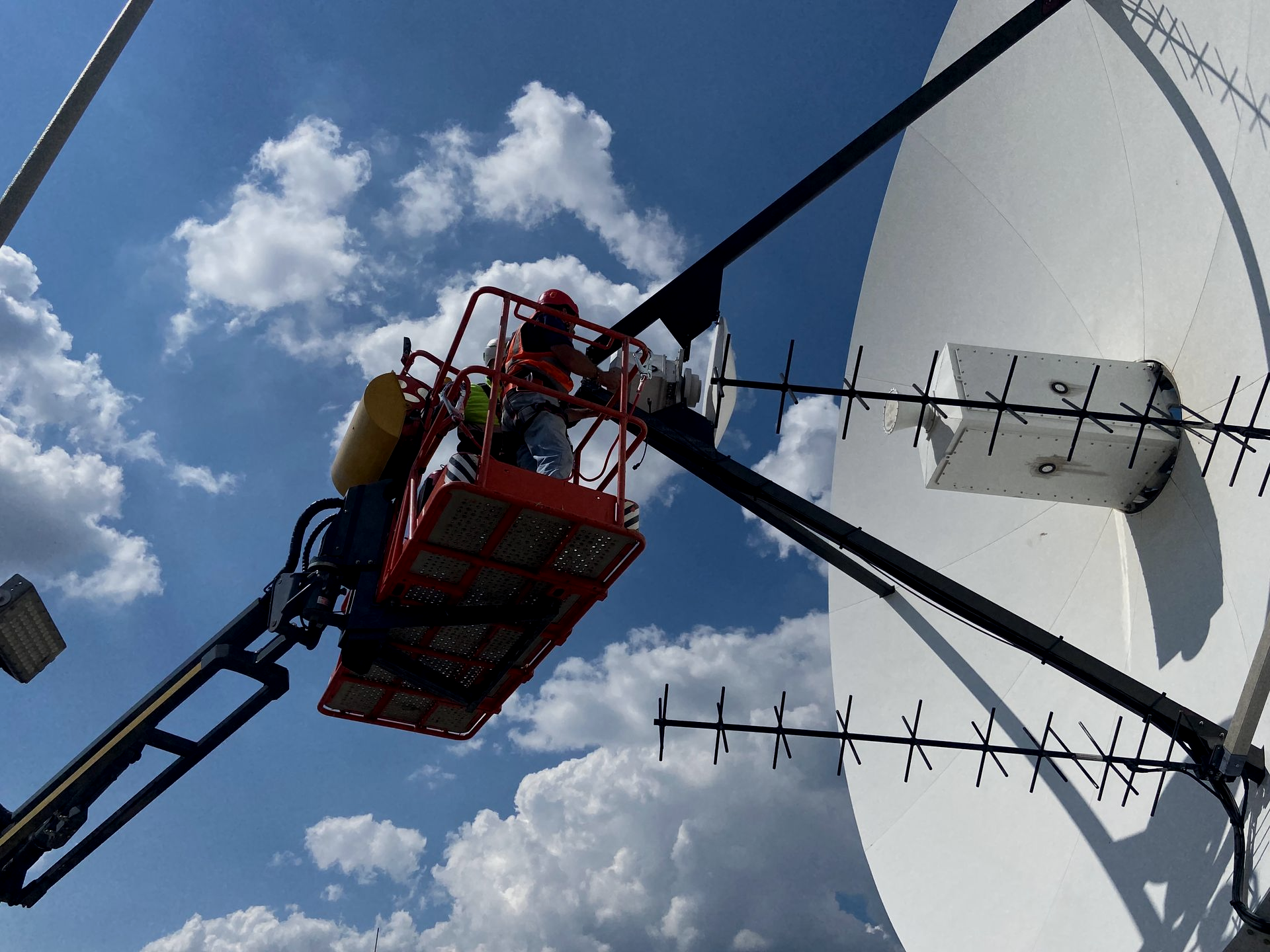 Working in high vis jacket in foreground with crane lifting antenna onto a high platform in background