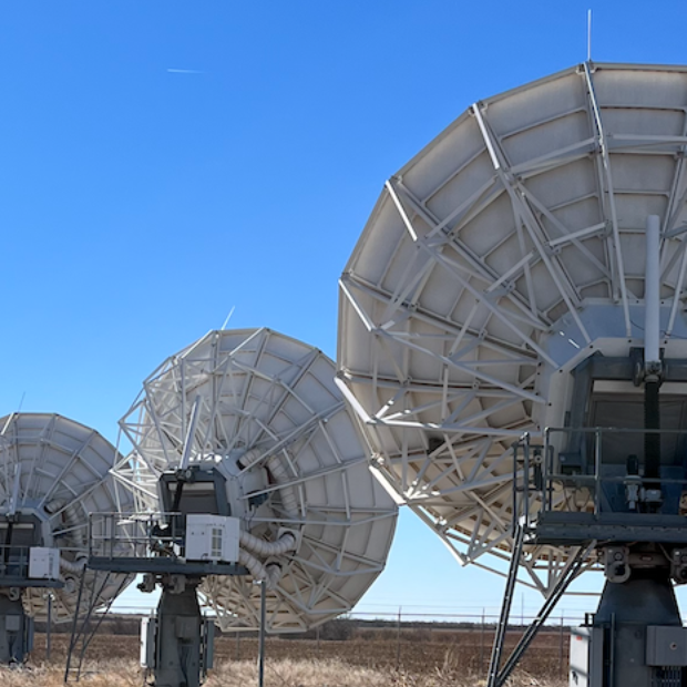 View of three satellite antenna dishes in a barren landscape with clear blue sky.