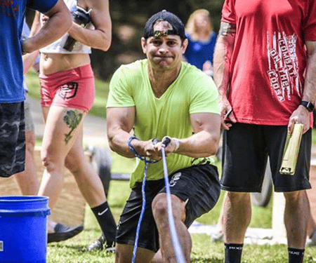 Man in neon green shirt pulling rope during a muddy outdoor tug-of-war event