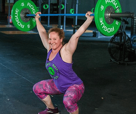 Weightlifter in purple lifting a barbell overhead in a gym, crouched in a squat