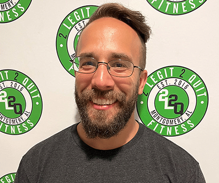 Smiling man with glasses and beard in front of a Legit 2.0 Fitness logo backdrop