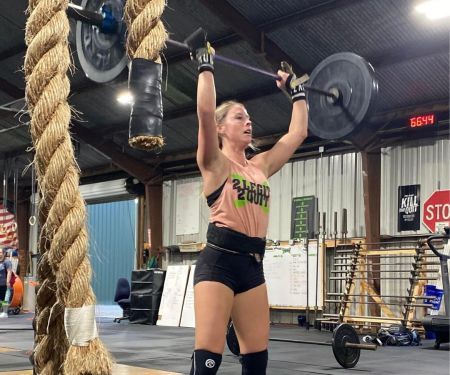 Athlete lifting a barbell overhead in a gym, with ropes and workout equipment in the background