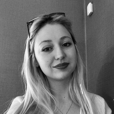 Woman with long blonde hair smiles at the camera, wearing sunglasses on her head, red lipstick.