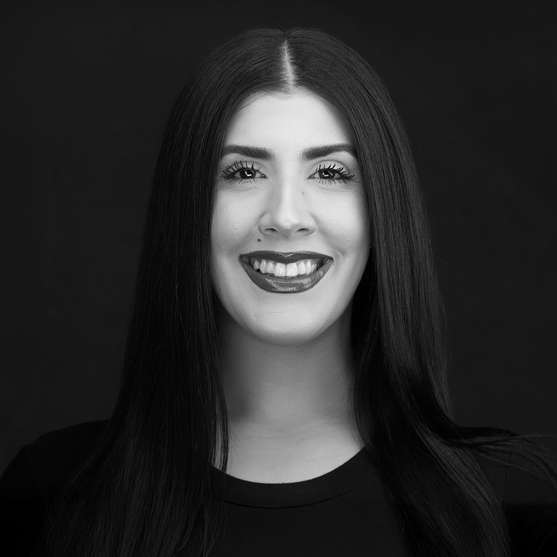 Woman with long dark hair, smiling, wearing dark lipstick. Maria at Hustlestop Newton MA