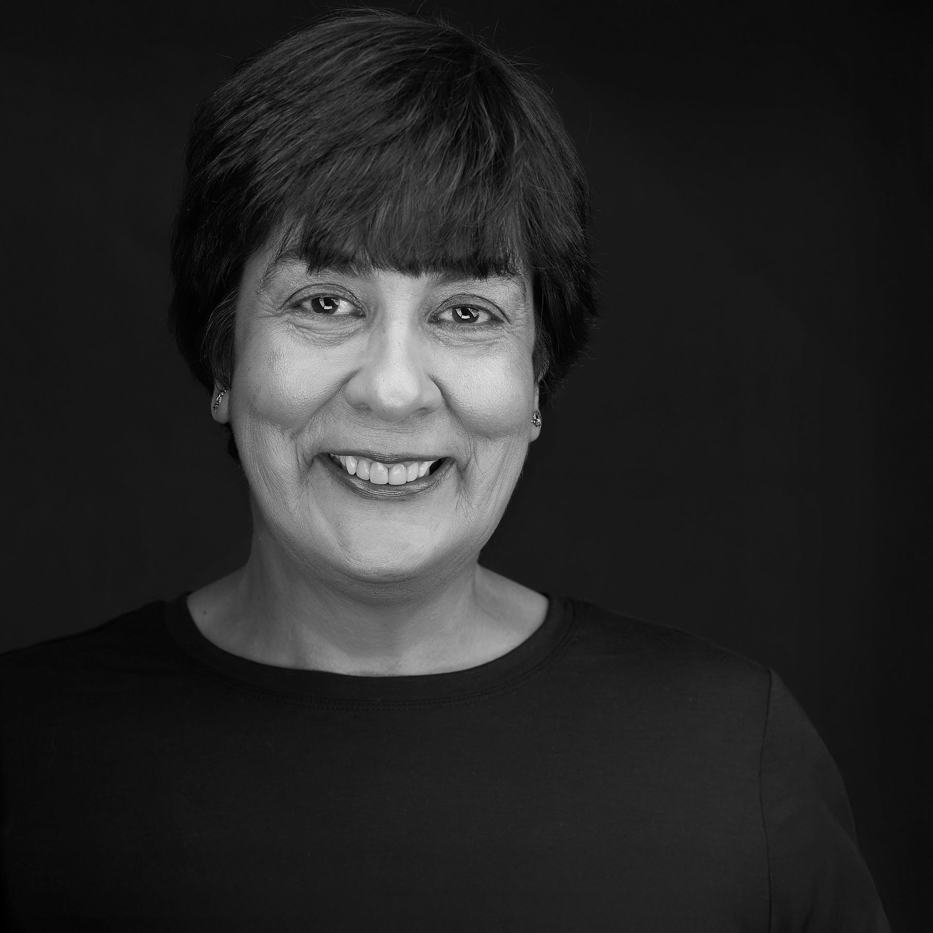 Smiling woman with short hair, patterned top, against leafy background.