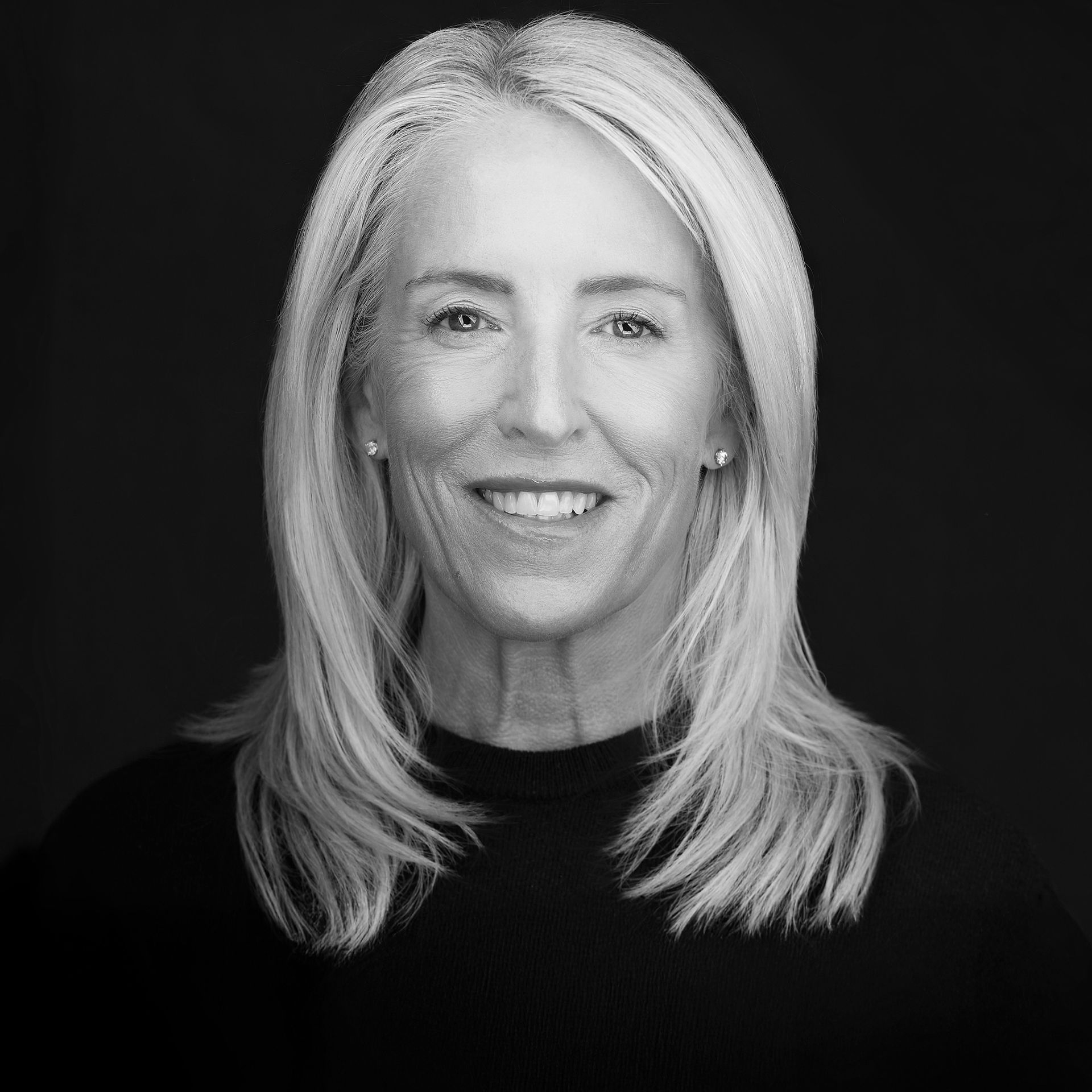 A woman in a plaid shirt is smiling in a black and white photo.