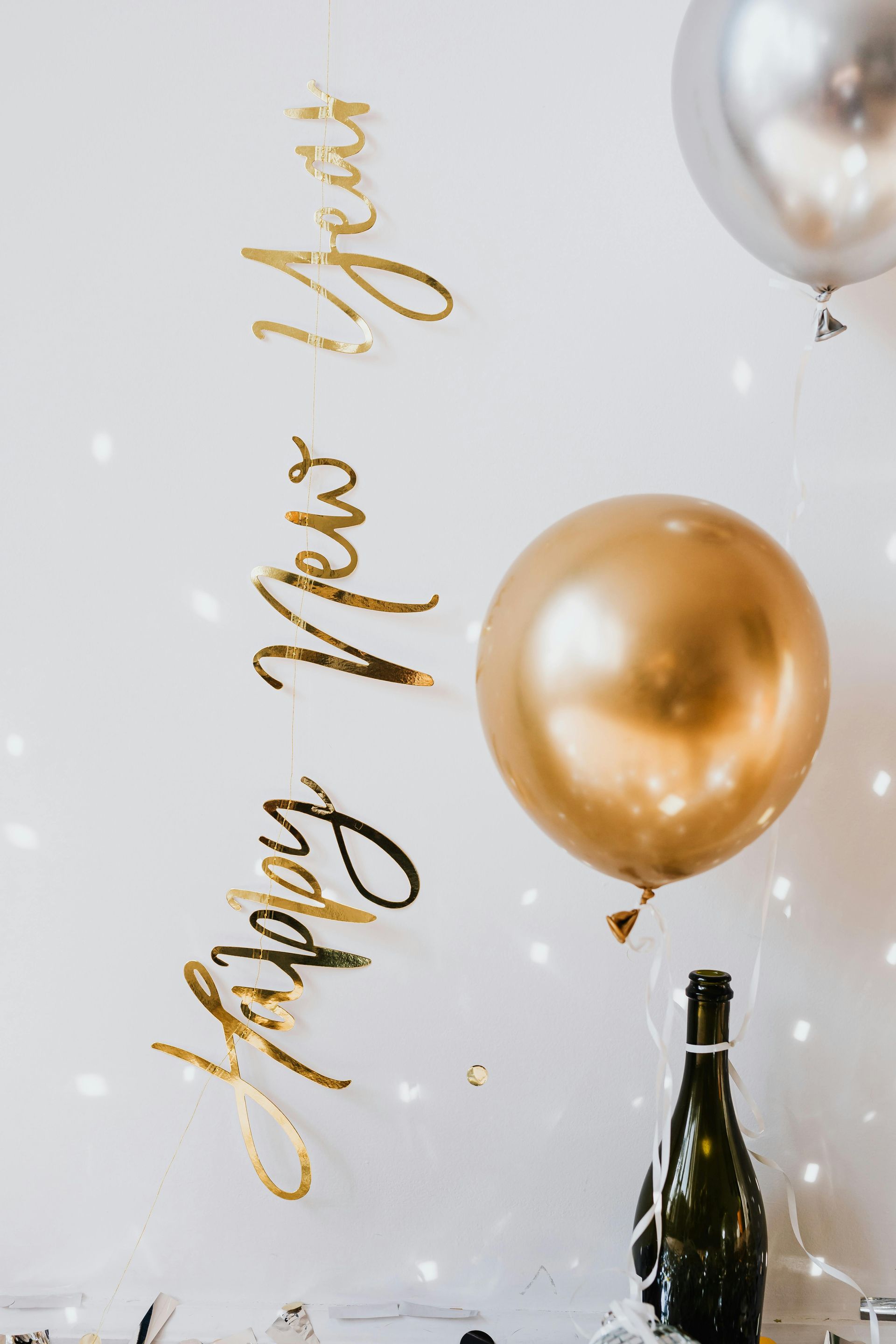 A bottle of wine , balloons , and a sign that says happy new year.