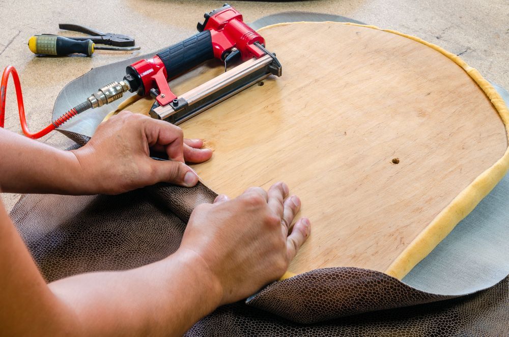 Hands Stapling Fabric to a Wooden Chair Seat With a Pneumatic Stapler — Atherton Decor Centre In Ravenshoe, QLD