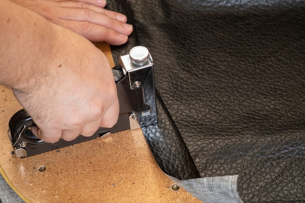 Person Stapling Black Leather to a Brown Wooden Frame Close Up — Atherton Decor Centre In Dimbulah, QLD