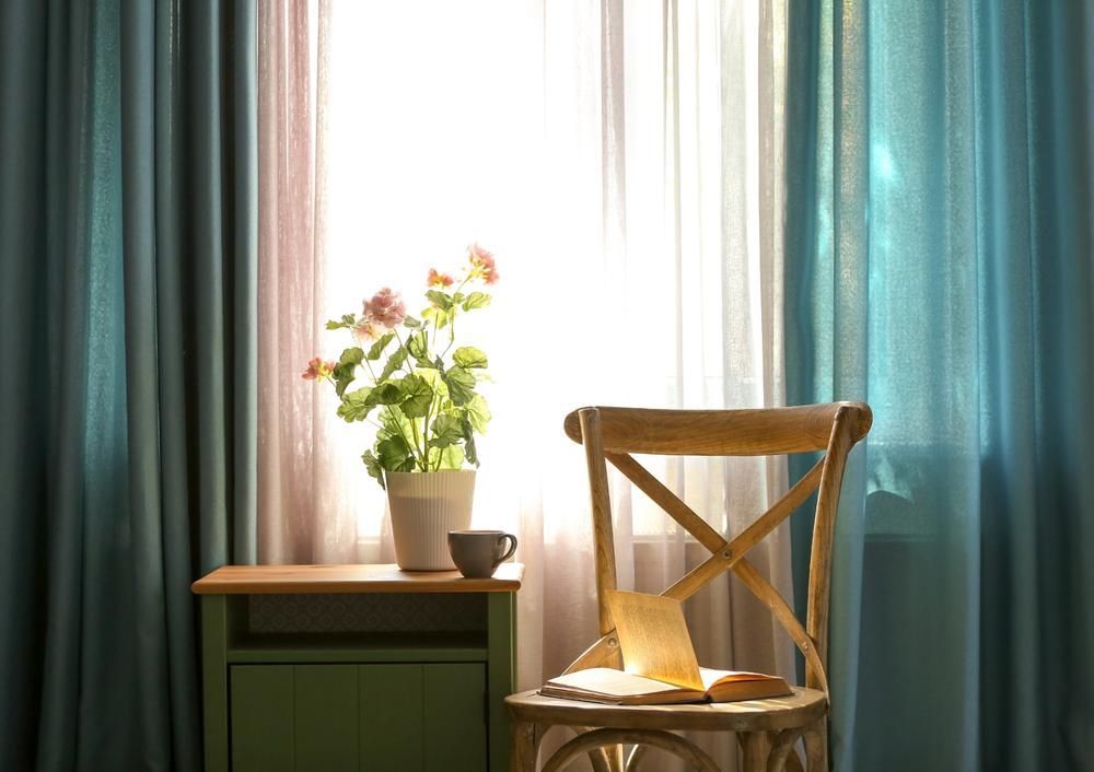 A Chair is Sitting in Front of a Window in a Room With Blue Curtain — Atherton Decor Centre In Tablelands, QLD