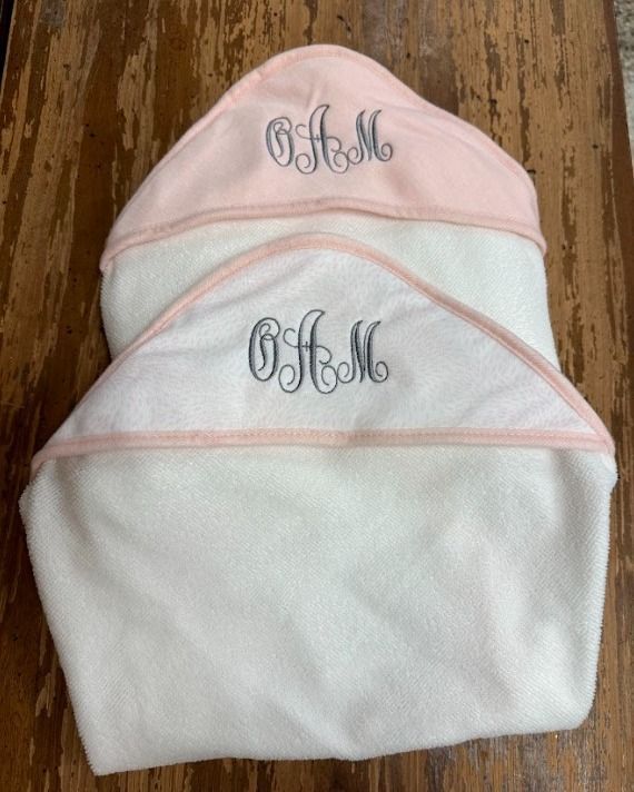 Two towels with monograms on them are sitting on a wooden table