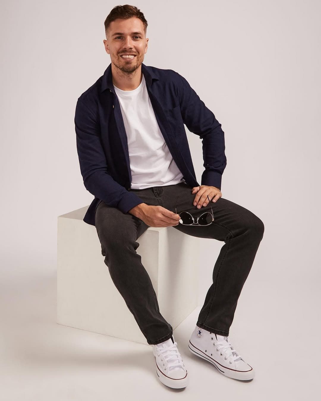 A Man is Sitting on a White Cube Wearing a Blue Jacket and White Sneakers — Bonanno's Menswear in Sutherland, NSW