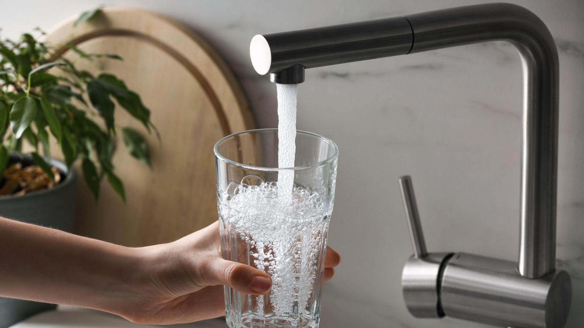 A person is pouring water into a glass from a faucet.