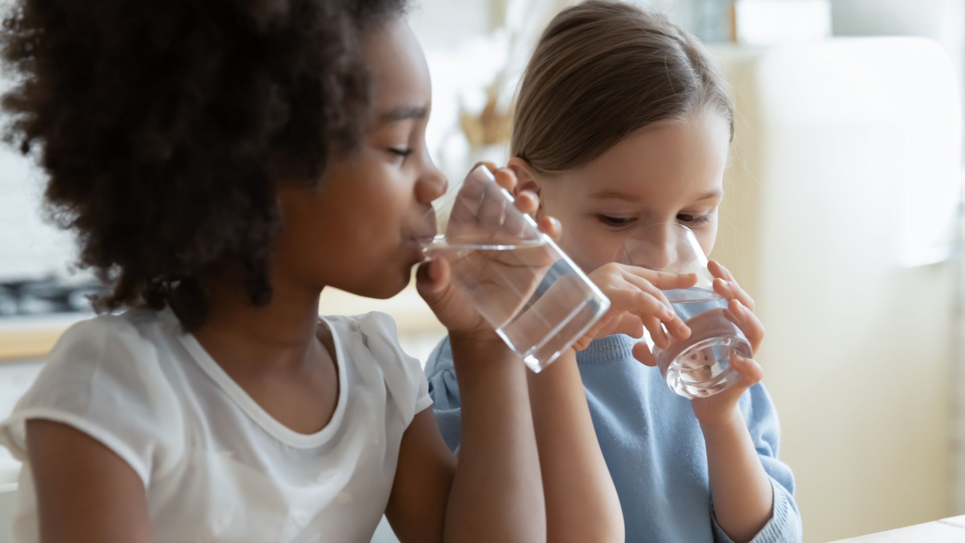 Two little girls are drinking water from glasses.