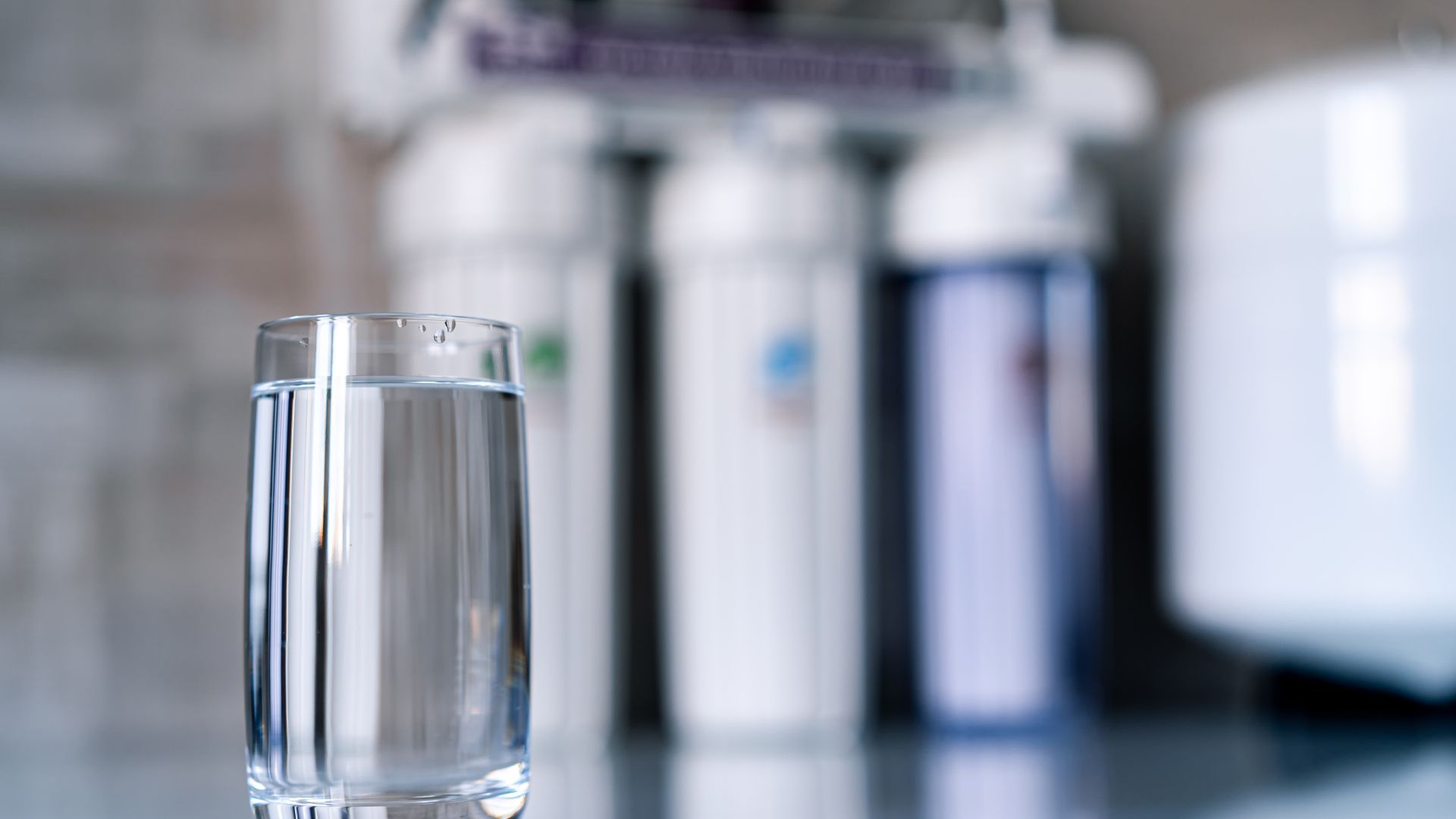 A glass of water is sitting on a counter in front of a water filter.