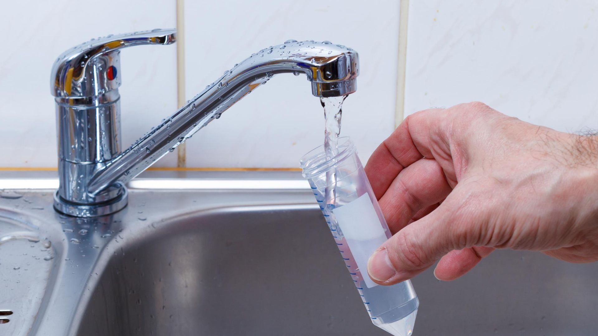 A person is pouring water into a measuring cup in a sink.