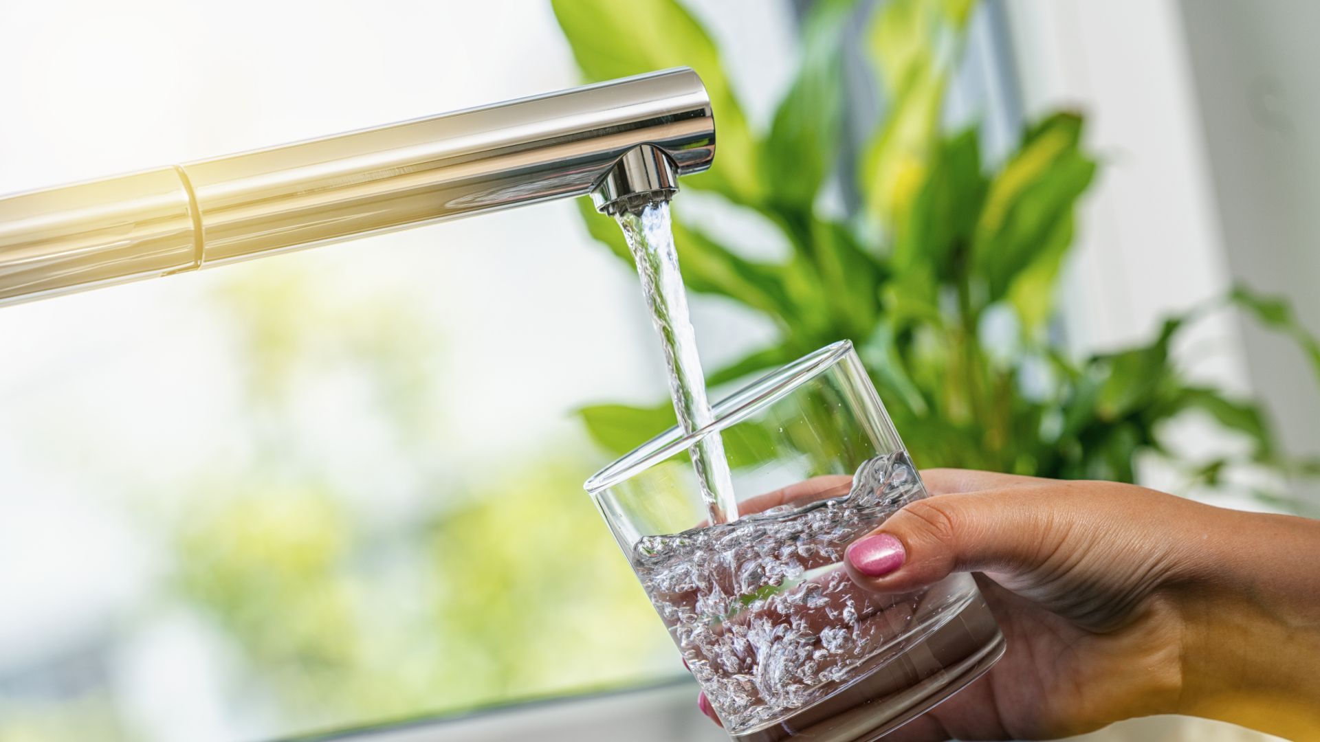 A person is pouring water into a glass from a faucet.