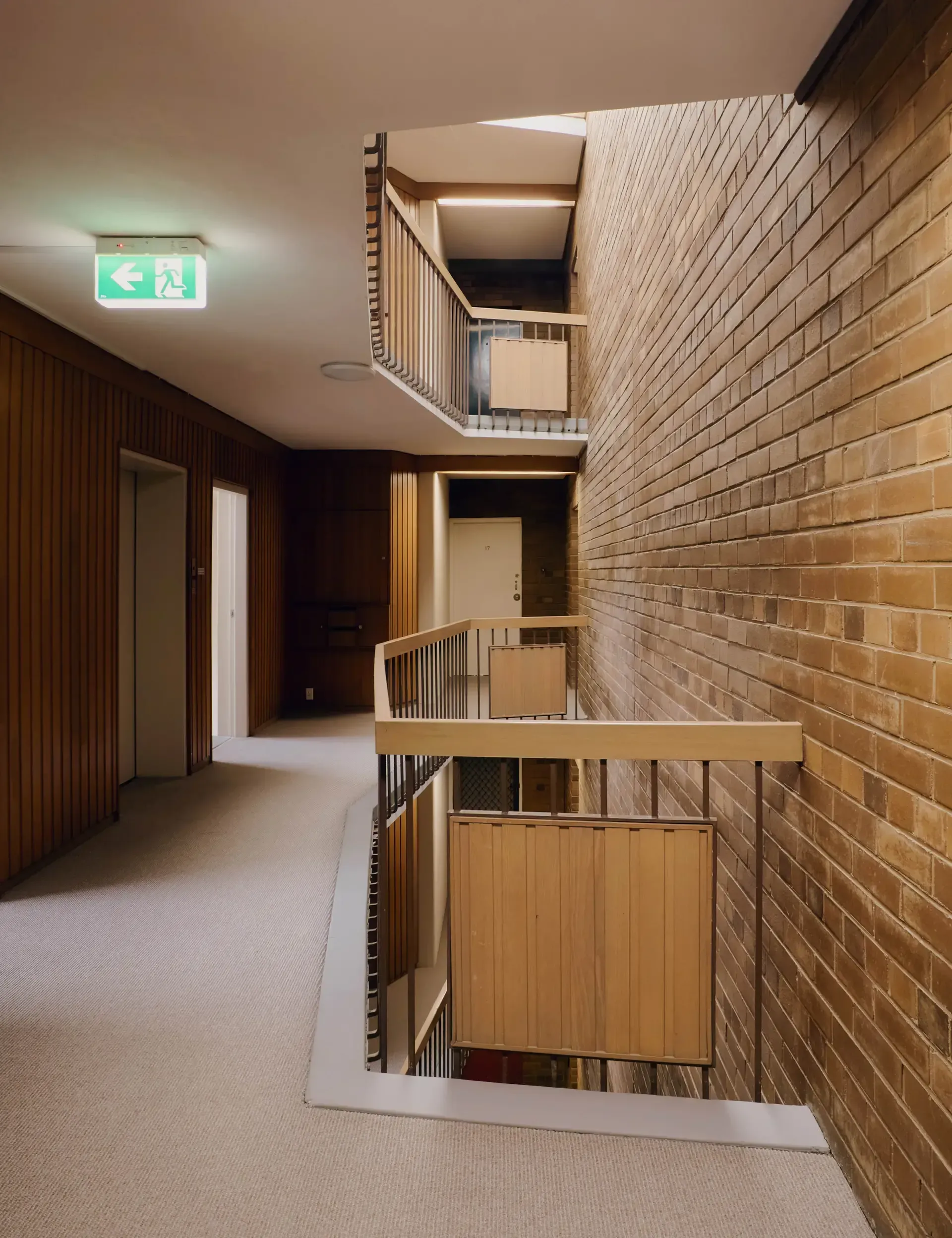 Hallway with carpet, wood paneling, and brick wall; staircase with wooden railings and cabinets.