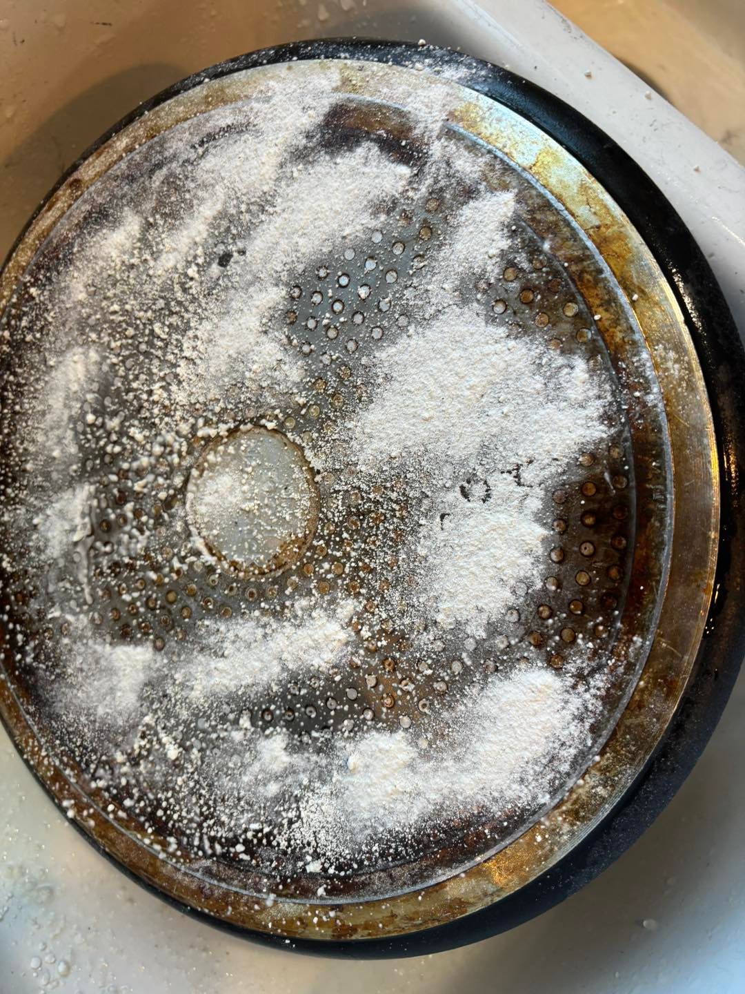 Black stovetop burner bottom covered in white powder.