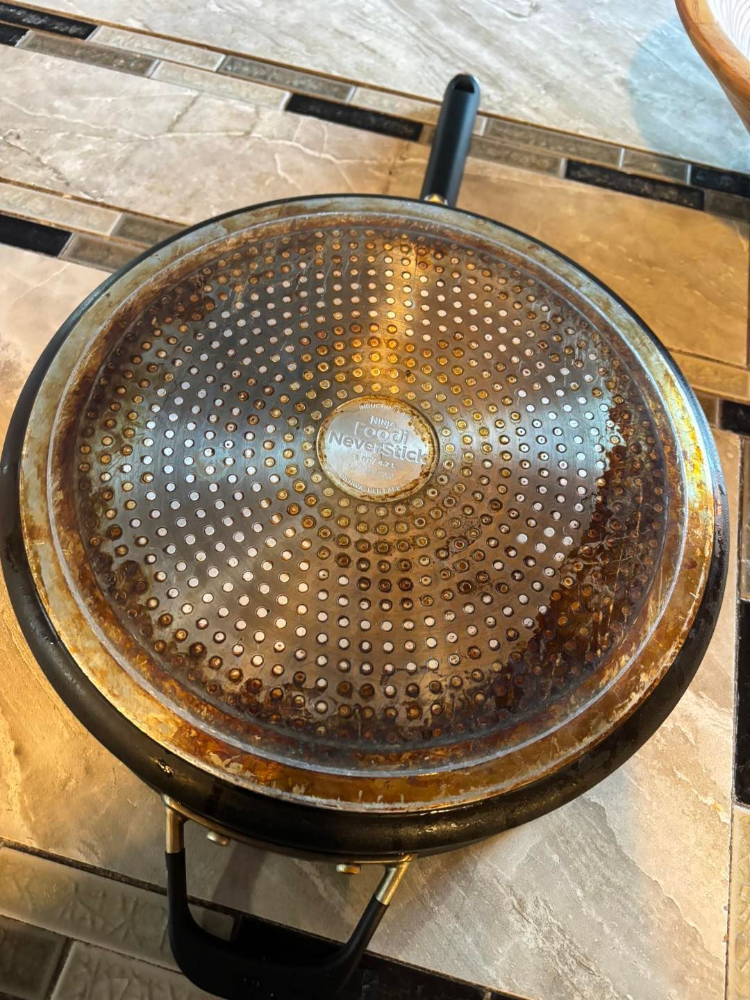 Close-up of a dirty skillet's underside, showing rust-colored stains and a patterned metallic surface.