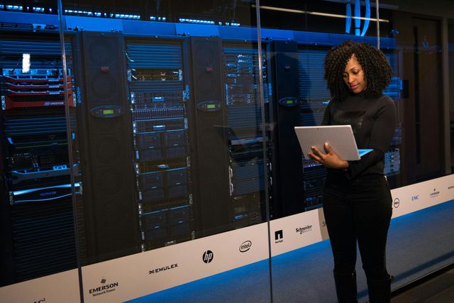 Woman using a tablet in a data center, monitoring servers; blue-lit environment.