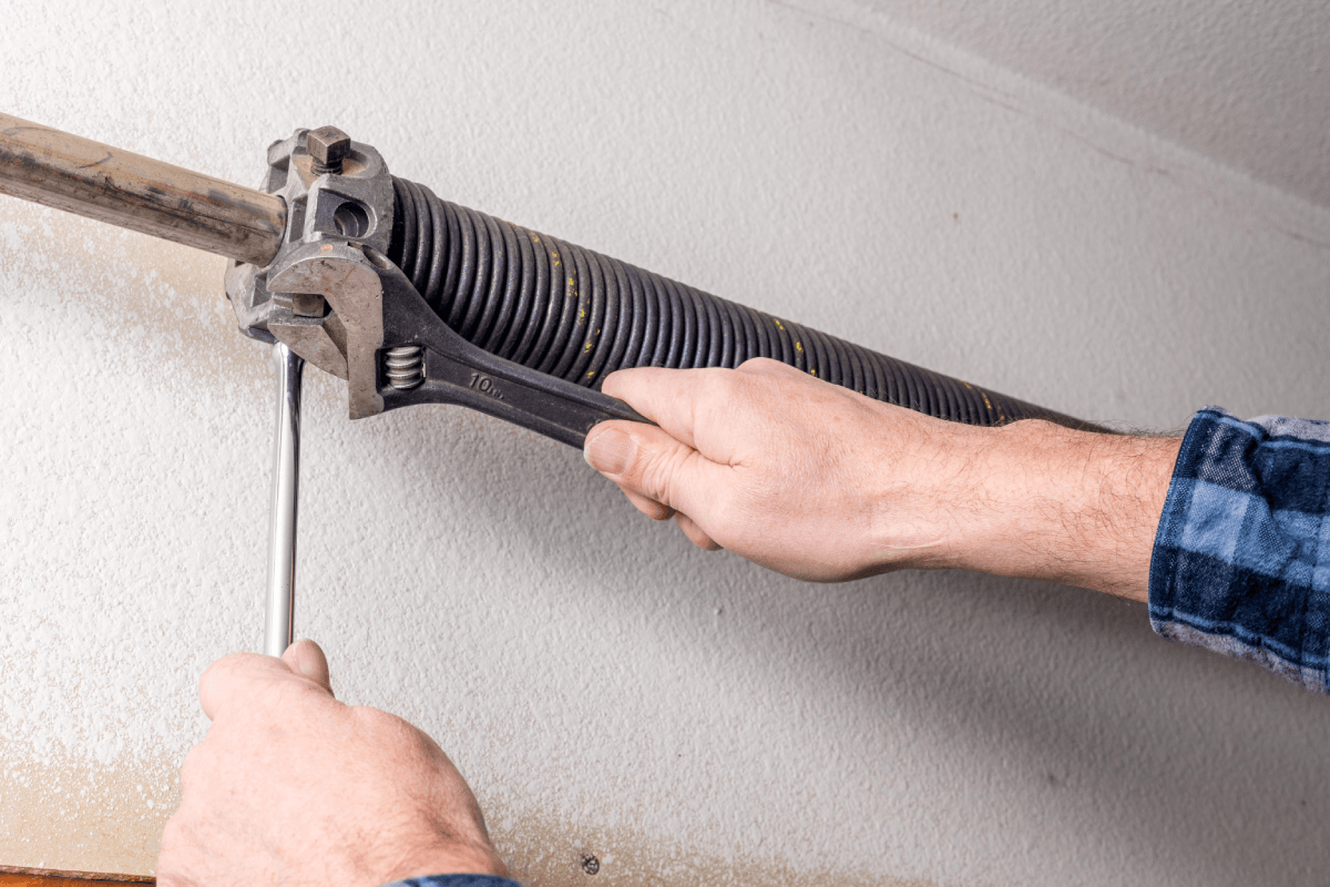 Garage door technician carefully adjusting an extension spring located along the horizontal track of the door.