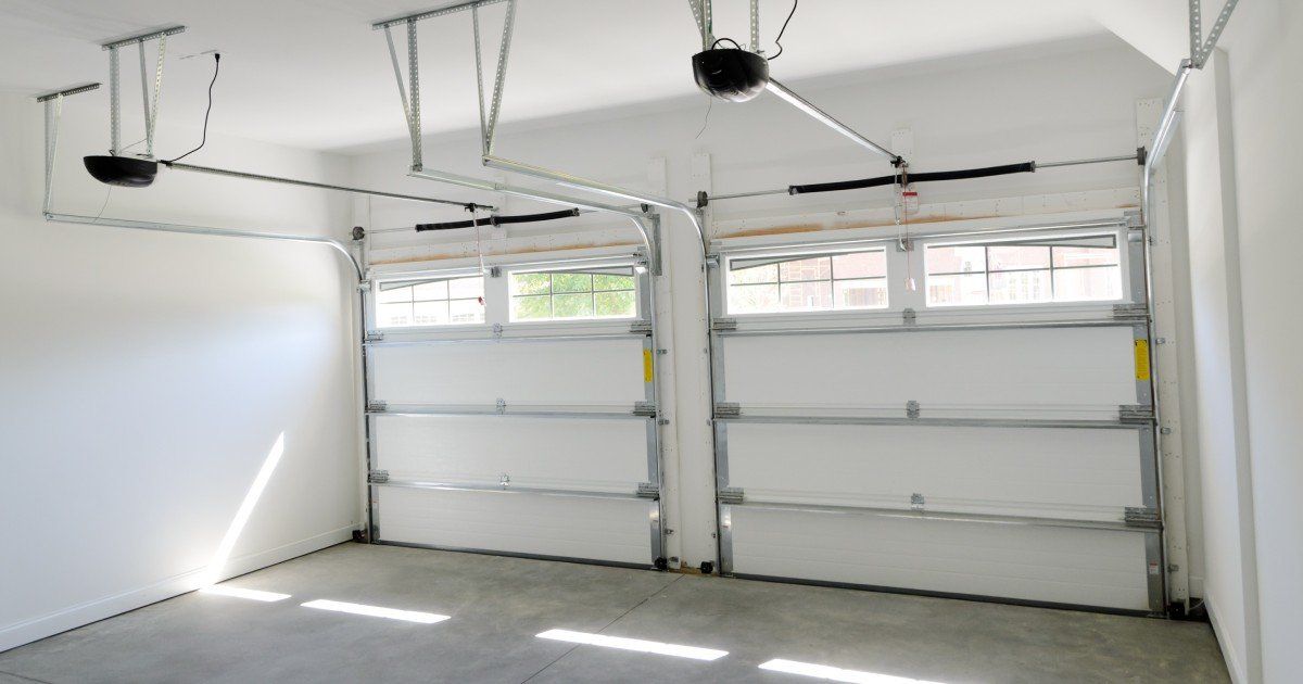 Interior of a modern garage with two automated sectional garage doors featuring metal tracks and window panels.