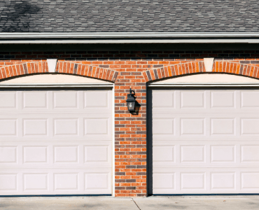 Two white garage doors on a brick building