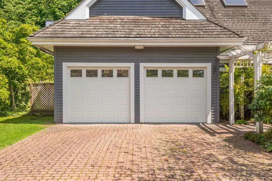 A garage with two white garage doors and a brick driveway.